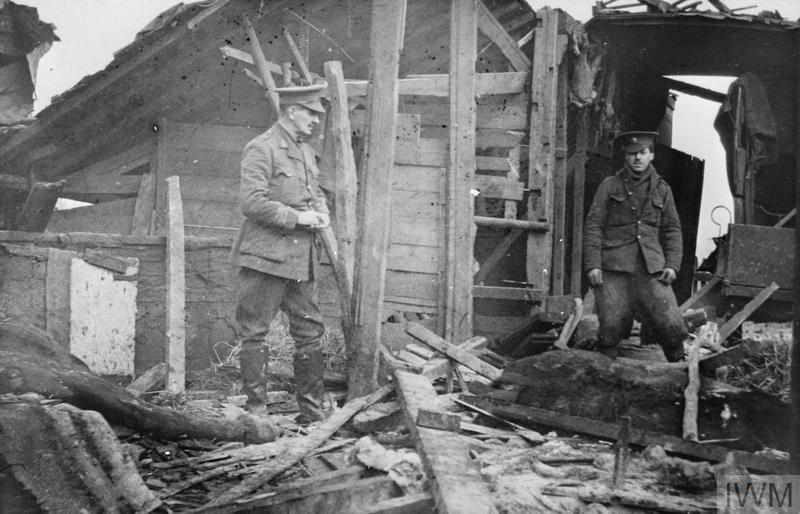 The effect of the first shell which landed in Erquinghem-Lys, November 1914. The stable was demolished and two horses (seen left and right) were killed. The driver, between them, who was grooming them at the time, was untouched. Lieutenant Colonel A A Watson, commanding officer of the 18th Field Ambulance, 6th Division, is in the centre. © IWM (Q 50226)