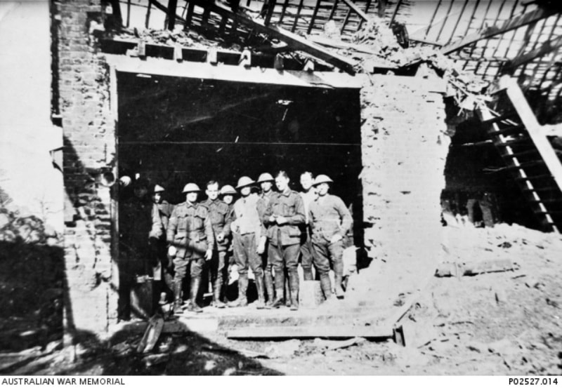 Le Bizet, France/Belgium border 1917. Members of 107th Australian Howitzer Battery standing in the remains of a bombed building. Note the siren mounted on the left wall of the building, possibly used for warning of gas shelling.